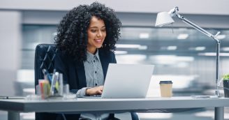 Modern Office: Black Businesswoman Sitting at Her Desk Working on a Laptop Computer. Smiling Successful African American Woman working with Big Data e-Commerce. Motion Blur Background
